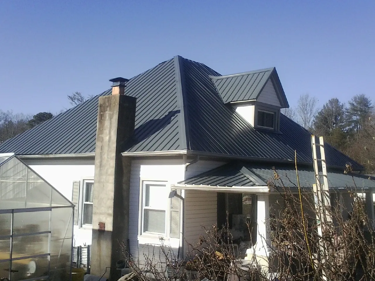 Dark blue standing seam metal roof on a white farmhouse with dormer — Slate & Tile Roof Repair by Roofing Brothers in Crabtree