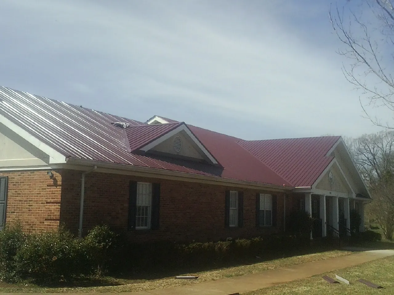 Red metal roof with gabled entries on a long brick building, from a Hail Damage Roof Repair job in Crabtree